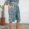 Person wearing a blue patterned outfit standing against a white wall with a cactus plant.