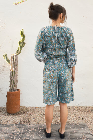 Woman wearing a floral outfit standing against a white wall with a cactus plant.