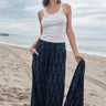 Woman at the beach wearing an ikat  low waist trousers, with white tank top and holding a matching jacket.
