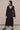 Woman wearing a black dress standing against a pink wall.