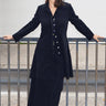 Woman standing outside wearing a black plush corduroy coat dress with a matching maxi skirt.