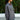 Woman wearing a gray shirt standing outdoors with greenery in the background