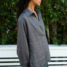 Woman wearing a gray shirt standing outdoors with greenery in the background