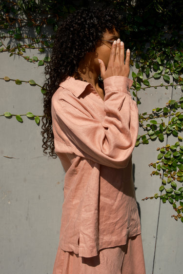Person wearing a pink outfit standing against a wall with greenery