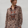 Woman wearing a patterned shirt and blue jeans against a white wall