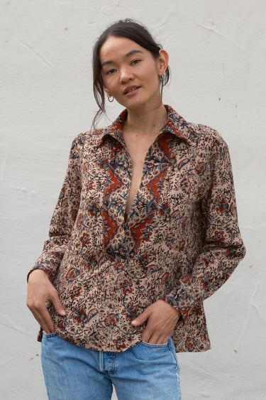 Woman wearing a patterned shirt and jeans against a white wall