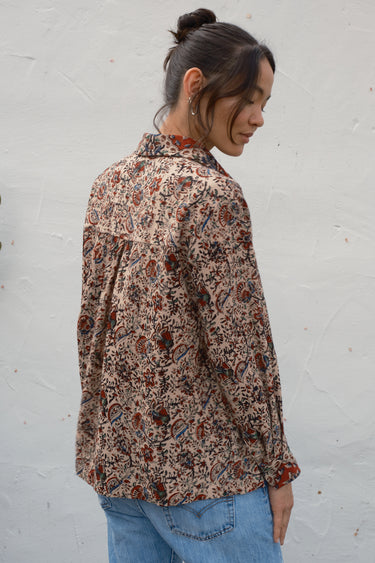 Woman wearing a patterned shirt and blue jeans against a white wall