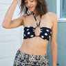 Letty band bikini top of black with white polka dots. worn with tapestry shorts. Standing in front of a green house with a white garage