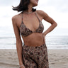 A woman standing on a beach wearing a floral woven triangle bikini top with sunglasses and a necklace.