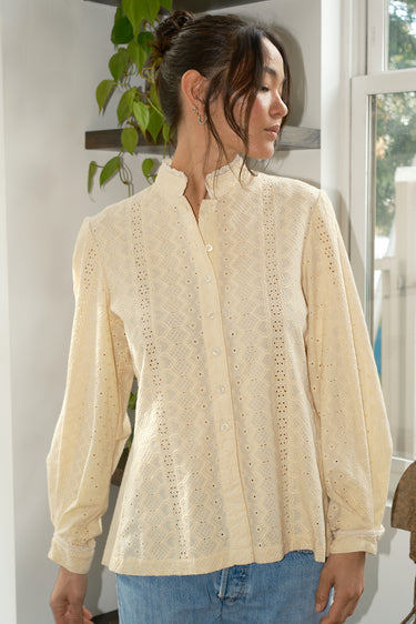 Woman wearing a cream-colored blouse with intricate patterns, standing indoors.