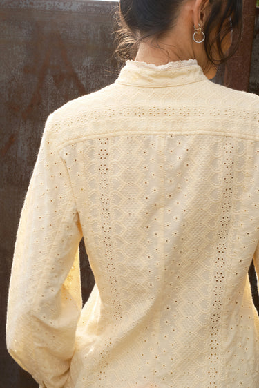 Close-up of a person wearing a cream-colored blouse with a textured pattern.