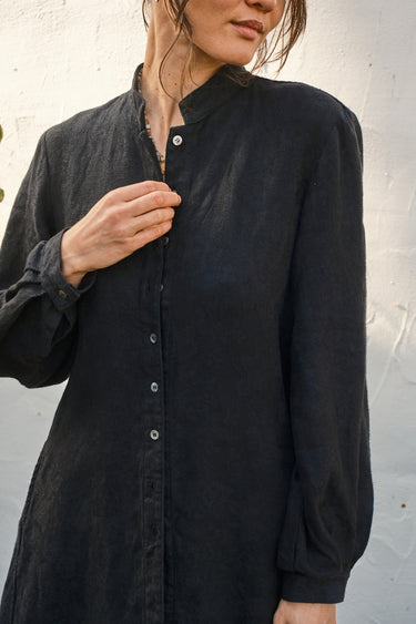 Person wearing a black button-up coat against a light gray background
