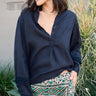 A woman wearing a black linen blouse with long sleeves and a band collar, paired with multicolored geometric patterned pants.