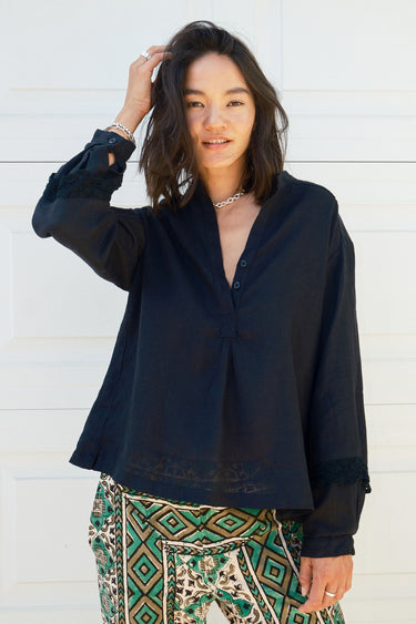A woman wearing a black linen blouse with long sleeves and a band collar, paired with multicolored geometric patterned pants.
