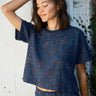 A woman standing with her hand raised to her head, wearing a navy blue woven tee top with a floral pattern and matching pants.