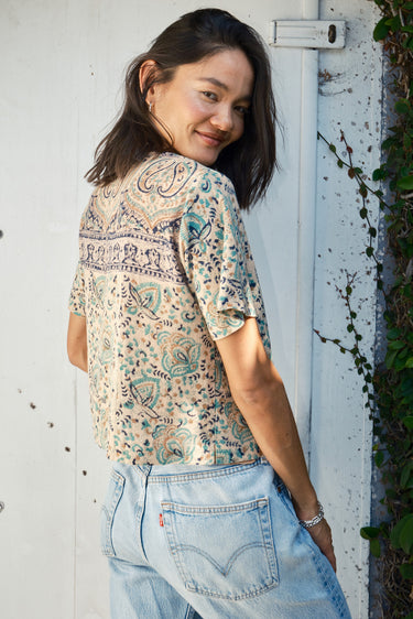 A woman wearing a beige and green hand woven and hand block printed Indian tapestry top with short sleeves and a round neckline.