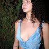 a woman standing in front of green trees wearing a light blue indigo dyed  corduroy bra top hand embroidered with many shades of blue thread. 