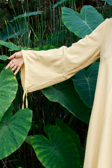 Person wearing a mimosa garment standing among large green leaves