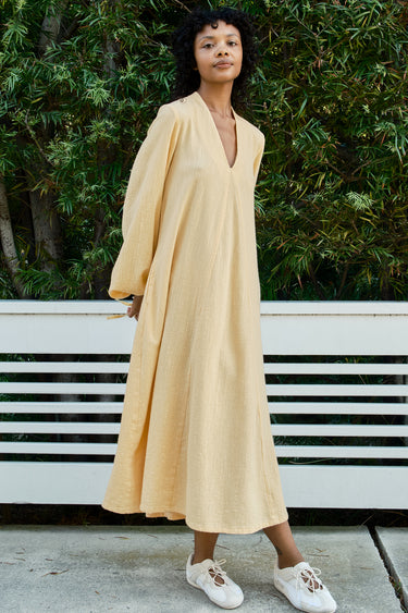 Woman wearing a yellow dress standing outdoors with greenery in the background