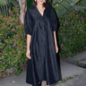 A woman standing outdoors wearing a long, black, balloon sleeve caftan with a V-neckline.