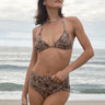 A woman standing on a beach wearing a floral bikini bottom and top with sunglasses and a necklace.