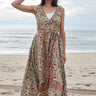 Woman standing on the beach wearing a red,  beige and green tapestry maxi wrap dress with a white tank underneath. 