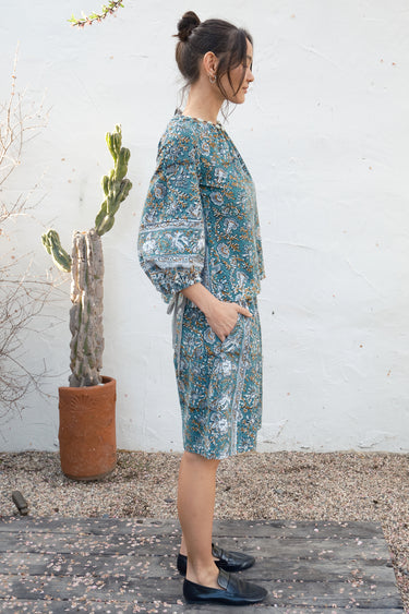 Woman in a floral blouse and short standing outdoors with a cactus plant in the background