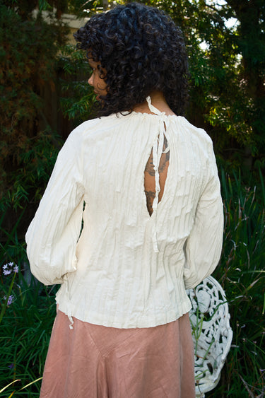 Person wearing a white blouse with long sleeves and a pink skirt in a garden setting