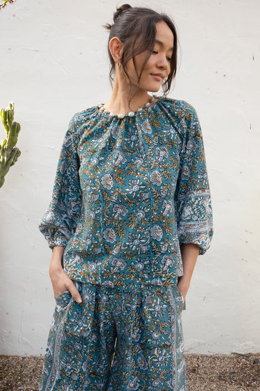 Woman wearing a blue floral dress standing against a white wall.