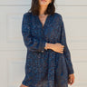 Woman standing in front of a white garage door wearing a navy blue tapestry mini shirt dress with long sleeves.