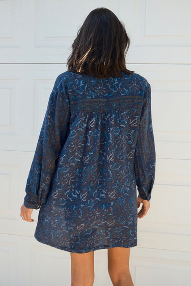 Back view of a woman standing in front of a white garage door wearing a navy blue tapestry mini shirt dress with long sleeves.