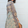 Woman  standing against a white garage door wearing a tan with green and black tapestry shirt caftan- dress, belted. 