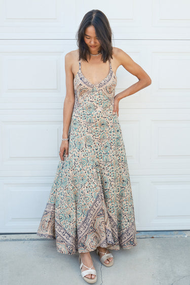 A woman standing in front of a white garage door, wearing a multicolored floral Nova slip dress. 