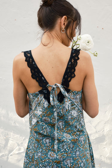 Woman wearing a floral dress with a lace back, standing against a light background.