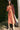 Woman in a persimmon dress standing outdoors with greenery in the background