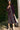Woman in a jet black dress standing outdoors with greenery in the background