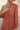 Person wearing a persimmon long-sleeve coat against a neutral background. detail