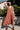 Woman wearing a persimmon colored dress  standing outdoors with greenery in the background