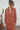 Woman wearing a persimmon colored outfit standing against a white wall with a cactus plant.