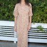 A woman standing outdoors wearing a blush calico tapestry maxi wrap dress with hand block printed tapestry design.
