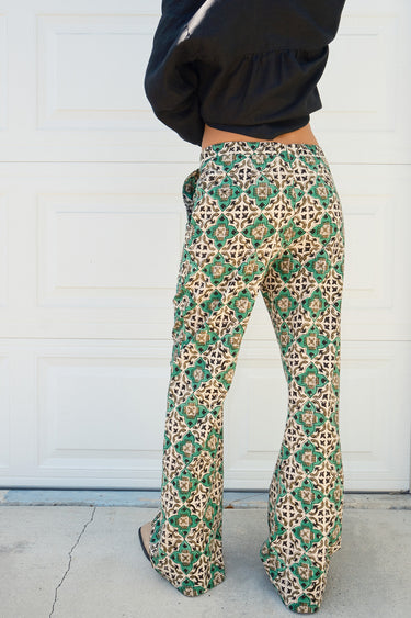 A person wearing a flare legged full length pant with a mid rise and a hand block printed Indian Tapestry design.
Worn with a black blouse 