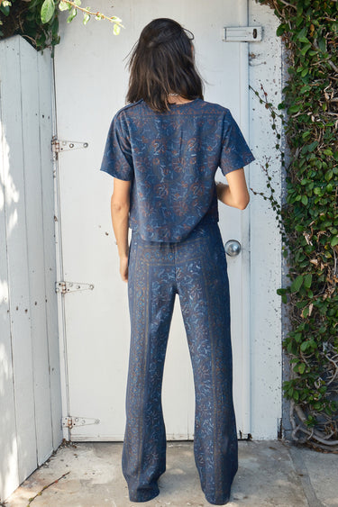 A person wearing a navy blue flare legged full length pant with a mid rise and hand woven, hand block printed Indian Tapestry. Back view