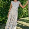 Woman in a floral dress standing against a green hedge