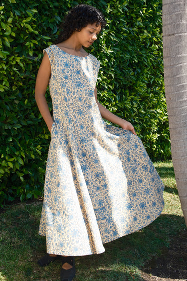 Woman wearing a floral dress standing against a green hedge