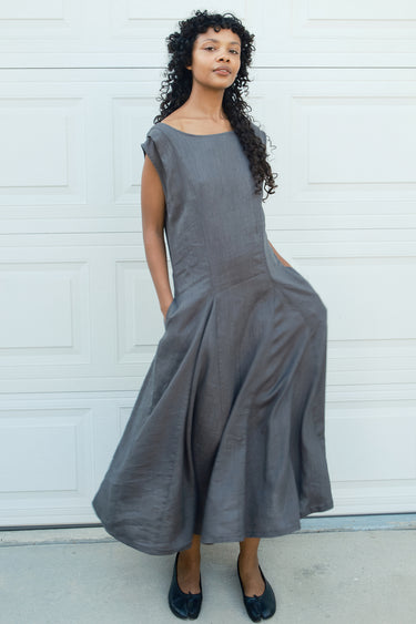 Woman wearing a gray dress standing against a white wall.