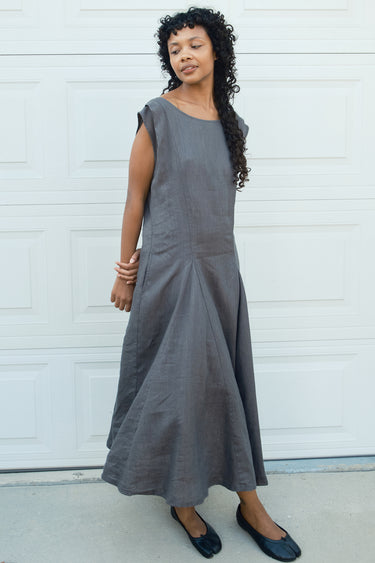 Woman wearing a gray dress standing against a white wall.