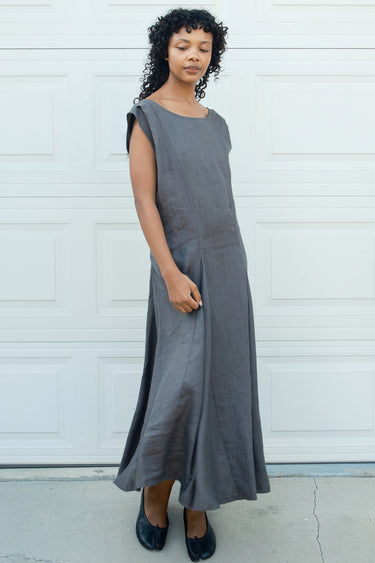 Woman wearing a gray sleeveless dress standing against a white wall.
