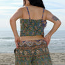 A woman standing at the beach wearing a floral tapestry low rise short cut using both green and blue tapestry of the same print tapestry mixed together features front pockets. Worn with a matching camisole.  Back View