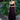 Woman in aNoire black  dress with yellow accents standing in front of green foliage.
