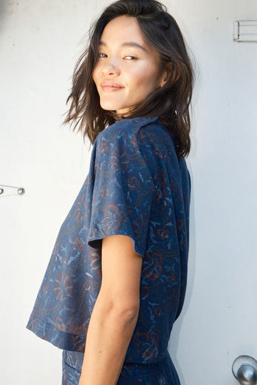 A woman  wearing a navy blue woven tee top with a floral pattern and matching pants.